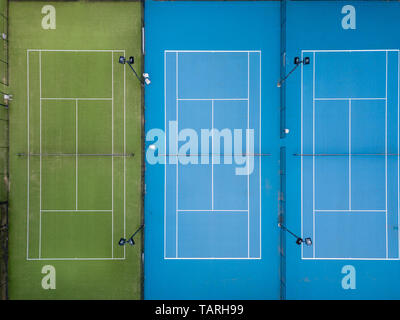 Antenne overhead Shot von drei Tennisplätze, Seite an Seite, keine Spieler, einem grünen Kunstrasen Hof und zwei blauen Hartplätze. Stockfoto