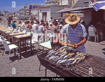 Nahaufnahme der historischen 1985 städtischen portugiesischen Archivansicht des Menschen Arbeiten beim Kochen Grill Sardine Fisch & Servieren von Lebensmitteln Gruppen von 1980s Urlaubsurlauber essen im Freien Stilvolles Café an Tischen im Freien am sonnigen Portimao Angeln Hafen & Kai in Algarve Portugal in "die Art, wie wir Waren' Archivbild 80s Stockfoto