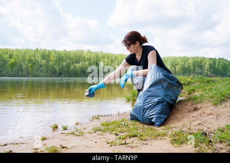 Foto der Frau in Gummihandschuhe Abholung Papierkorb am Ufer im Sommer Stockfoto