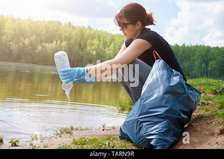 Foto der Frau in Gummihandschuhe mit schmutzigen Kunststoff Flasche in der Hand am Ufer im Sommer Stockfoto