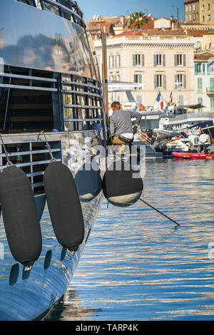 CANNES, Frankreich - April 2019: Personen, die mit einer Plattform, die über die Seite einer Superyacht in Cannes das Boot für den Sommer vorbereiten Stockfoto