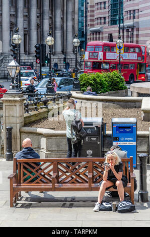 Touristen sitzen auf Holzbänken im Royal Exchange, London. Eine Dame hält und schaut auf ihr Mobiltelefon. Stockfoto