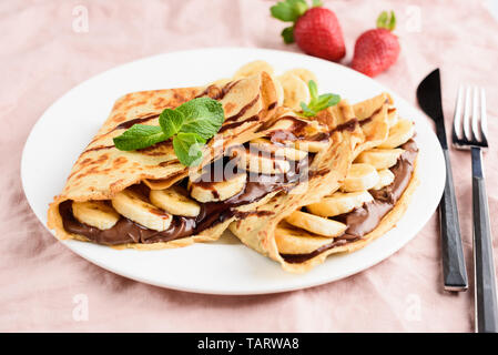Mit Schokolade und Banane auf weiße Platte auf rosa Hintergrund Krepp. Leckere Dessert Stockfoto