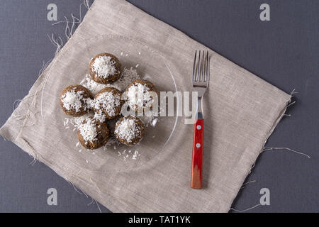 Gesunde bio Energie Kugeln mit Datteln, Backpflaumen, Rosinen, Erdnüsse, mit Kokos Späne, in einer Platte auf grauem Hintergrund, flach. Stockfoto