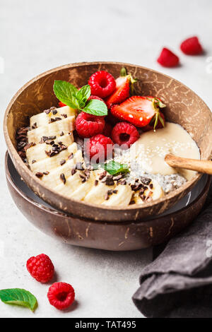 Chia Milchreis mit Beeren, Banane, Erdnussbutter und Kakaokerne in einer Kokosnuss Schale Schüssel. Stockfoto