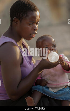 Mutter Flasche Ihr Baby füttern, auf dem Boden sitzend und draußen im Sonnenlicht Stockfoto