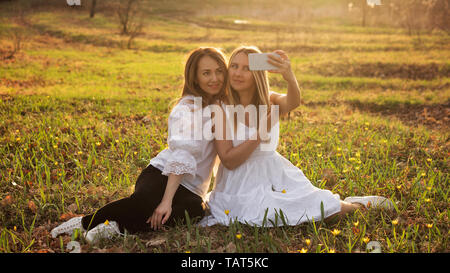 Schwestern sitzen in eine sonnige Wiese und unter selfie auf einem Smartphone. Family Portrait. Frauen Freundschaft. Verwandten Stockfoto