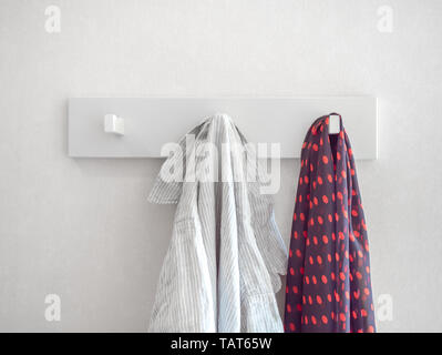 Entspannt weiss gestreiftes Hemd und red Polka Dot Pattern Schal an den Weißen Moderne Aufhängevorrichtung für weiße Wand im Hintergrund. Stockfoto