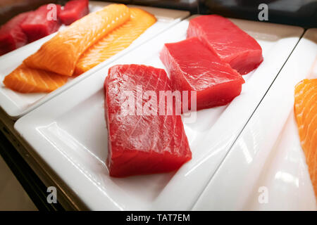 Drei große Stücke von Thunfisch und Lachs für Sushi liegen auf einem weißen Teller in der Kühltheke. Stockfoto