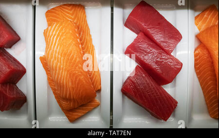 Mehrere große Stücke von Thunfisch und Lachs für Sushi liegen auf einem weißen Teller in der Kühltheke. Stockfoto