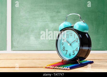 Wecker und Buntstifte auf Holztisch mit schiefertafel Hintergrund. Zurück zu Schule Konzept Stockfoto