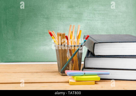 Stapel Bücher mit Stift und Papier mit Bleistift im Korb Container auf Holztisch mit schiefertafel Hintergrund. Zurück zu Schule Konzept Stockfoto