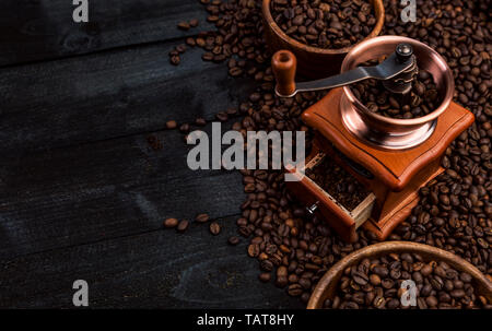 Gemahlener Kaffee, Kaffee Mühle, Schüssel gerösteten Kaffeebohnen auf schwarzem Holz- Hintergrund, Ansicht von oben Stockfoto