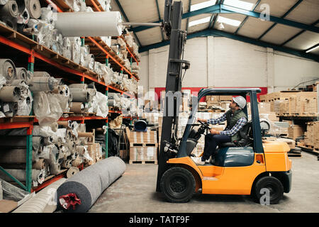 Gabelstapler Fahrer vorsichtig auf Vorrat aus den Regalen während der Arbeit auf dem Boden eines großen Teppich Lager Stockfoto