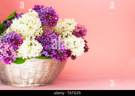 Lila Blumen Strauß in einem Korb auf unscharfen Coral Pink backgrond. Wunderschön duftenden Flieder Blumen Blumenstrauß mit Platz kopieren. Der Frühling noch leben. Stockfoto