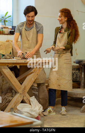 Grundlagen der Töpferei. Freundliche gutaussehende Paar verbringen Zeit in der Werkstatt, während mit Händen bedeckt in Ton. Stockfoto