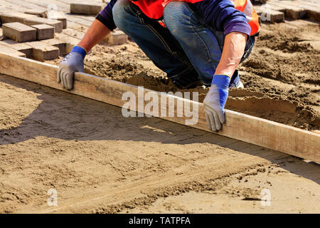 Der Arbeitnehmer richtet die Stiftung mit einem hölzernen Ebene fortzusetzen und ebnet ebnet. Stockfoto