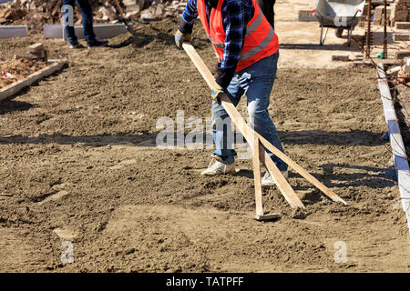 Der Arbeitnehmer richtet die Stiftung mit einem Holz- Ebene zu beginnen verlegen Pflastersteine auf der Arbeitsfläche. Stockfoto
