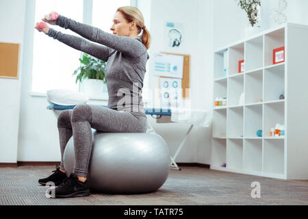 Fitness Training. Nette gut aussehende Frau sitzt auf der med-Ball beim Fitness- und Lauftraining Stockfoto