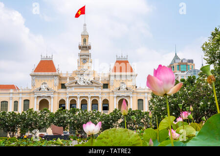 Stadt Halle (Saigon oder Ho Chi Minh City People Committee) mit Pink Lotus Blumen und blühende Plumeria Bäumen im Vordergrund (unscharf). Stockfoto