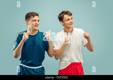 Zwei junge Männer stehen in Sportbekleidung auf Blau studio Hintergrund isoliert. Der Sport Team Fans. Schönen männlichen Modelle Brustbild. Konzept der Hum Stockfoto