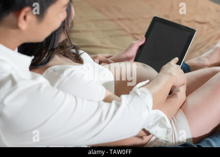 Close up Paar schwangere Frau und Mann sucht Tablet in der Hand, auf dem Bett Hintergrund. Stockfoto