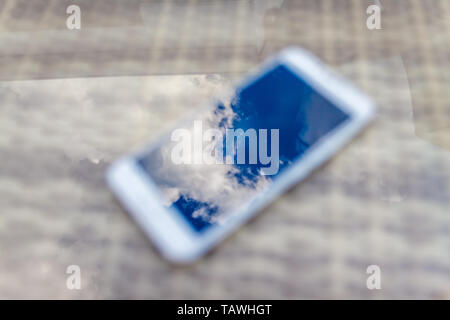 Reflexion der blauen Himmel mit Wolken im Telefon - Smartphone, das auf einem hellen Rattanmöbeln Tabelle vor dem Hintergrund liegt. Blur und Abstraktion Stockfoto