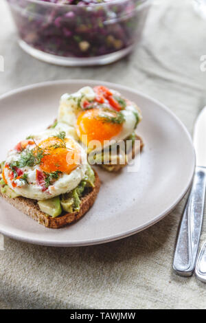 Frühstück serviert von zwei Toasts mit Avocado, Spiegelei mit Gemüse und Kräutern auf einem rustikal Tischdecke Hintergrund. Blick von oben. Gesunde und Nutr Stockfoto