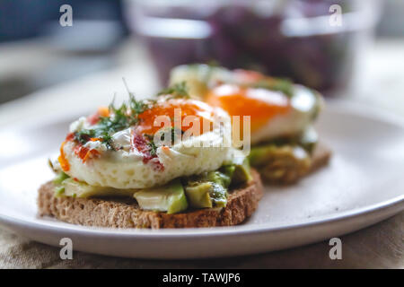 Frühstück serviert von zwei Toasts mit Avocado, Spiegelei mit Gemüse und Kräutern auf einem rustikal Tischdecke Hintergrund. Blick von oben. Gesunde und Nutr Stockfoto