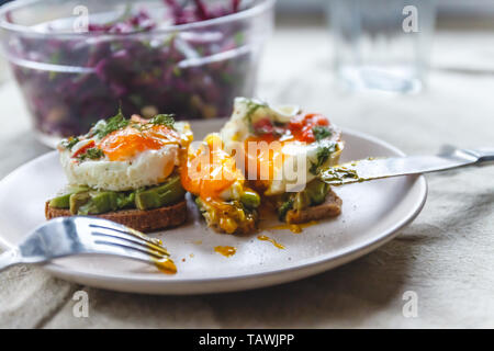 Frühstück serviert von zwei Toasts mit Avocado, Spiegelei mit Gemüse und Kräutern auf einem rustikal Tischdecke Hintergrund. Blick von oben. Gesunde und Nutr Stockfoto