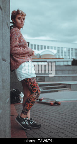 Schöne junge Mädchen mit Tätowierungen mit dem Longboard in der Stadt. Sie hat die traditionelle japanische tattoo Stockfoto