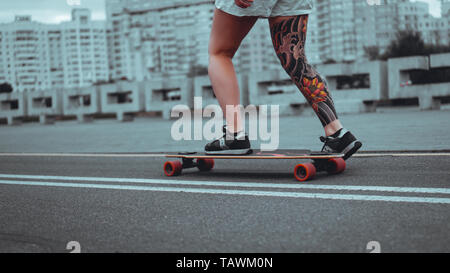 Schöne junge Mädchen mit Tätowierungen mit dem Longboard in der Stadt. Sie hat die traditionelle japanische tattoo Stockfoto