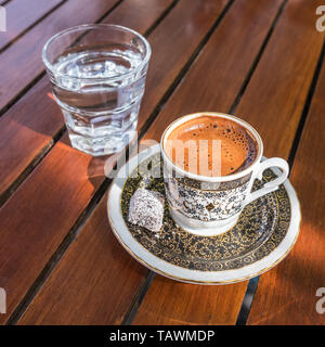 Traditionell starken und dunklen türkischen Kaffee, serviert mit einem Glas Wasser auf einer Seite an einem hölzernen Tisch in Café im Freien Stockfoto