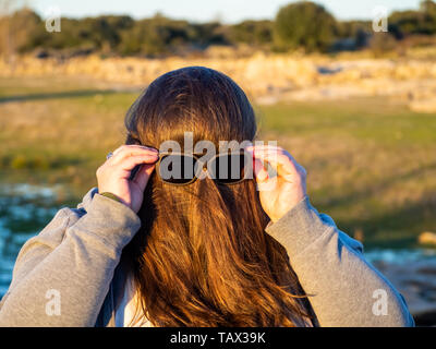 Eine kurvige Frau, die lustige Gesten mit Haar vor seinem Gesicht und Sonnenbrille Stockfoto