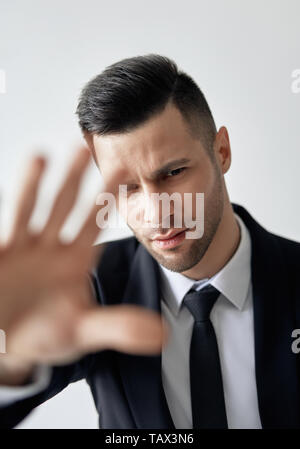 Schöner Mann im Anzug mit STOP-Schild auf weißem Hintergrund Stockfoto