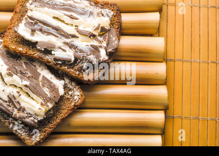 Sandwich mit grober, schwarzer Korn Brot und süßen Quark und dunkler Schokolade auf einem Bambus stehen und Bambus Serviette. Lecker einfach gesundes Frühstück in Th Stockfoto