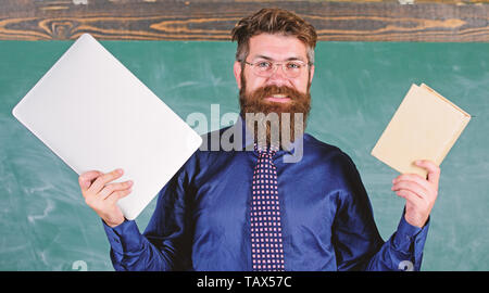 Digitale gegen Papier. Lehrer bärtigen Hipster hält Buch und Laptop. Was würden Sie bevorzugen. Lehrer mit modernen pädagogischen Ansatz. Buch aus Papier gegen Laptop. Mit der rechten Lehre Methode wählen. Stockfoto