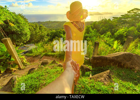 Folgen Sie mir. Touristische Frau im gelben Kleid die Hand des Partners auf die Seychellen, Indischer Ozean. Spektakuläre Aussicht auf Praslin von oben Blick auf La Digue Stockfoto