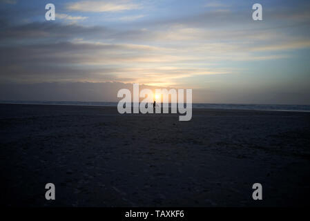 Wunderschöne, ruhige und gelassene Bilder der Landschaft mit einer Person in Silhouette ein Pferd Reiten entlang der Küste am Strand bei Sonnenuntergang Stockfoto