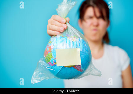 Frau hält in den Händen Plastikbeutel mit leeren Aufkleber und Planeten Erde mit blauen Hintergrund. Stockfoto