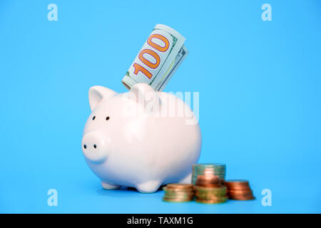 Bild auf der Seite des Schweins Sparschwein mit Münzen und Banknoten auf leeren blauen Hintergrund Stockfoto