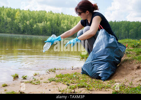 Bild der Frau in Gummi Handschuhe mit schmutzigen Kunststoff Flasche in der Hand auf der Bank Stockfoto