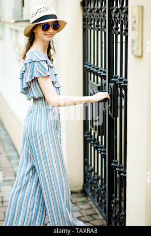 Attraktive Mädchen in Overall Kleid ist öffnung Schwarz geschmiedete Tore, Seitenansicht Stockfoto