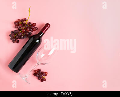 Eine Flasche Wein ein leeres Glas aus einem Bündel von roten Trauben auf einem sanften rosa Hintergrund. Flache layout Ansicht von oben. Kopieren Sie Platz. Stockfoto