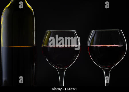 Wein. Rotwein in zwei Weingläser auf dunklem Hintergrund. Silhouette der Flasche mit Rose Wein Stockfoto