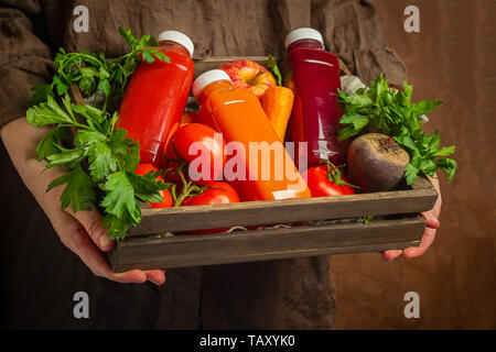 Frische Säfte Smoothies aus verschiedenen Gemüse Karotte apple Zuckerrüben, Tomaten in Flaschen in einer Holzkiste in weibliche Hände. Stockfoto