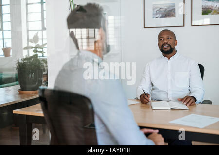 Lächelnd African American Office Manager führt ein Interview mit einem potentiellen neuen Mitarbeiter an seinem Schreibtisch in einem Büro Stockfoto