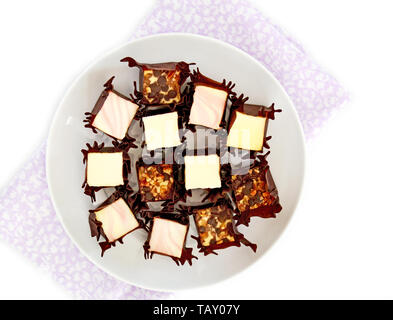 Vanille, Raspberry Swirl und Walnuss Chocolate Chip mini Käsekuchen beißt in dunklen Wrapper auf runde weiße Platte auf weißem Hintergrund. Stockfoto