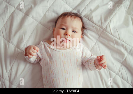 Portrait von cute adorable Asiatischen gemischten Rennen Baby Mädchen vier Monate alten liegend auf Bett im Schlafzimmer in Kamera schaut. Blick von oben über. Kindheit Diversi Stockfoto