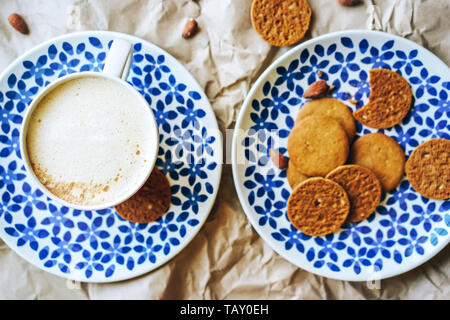 Layout mit einer großen Tasse Cappuccino und peanut Cookies auf blau gemusterten Platten mit blauem Muster, gesundes und leckeres Frühstück. Stockfoto